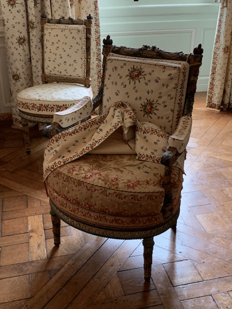 Fauteuil de la collection « aux épis » de la chambre de Marie-Antoinette au Petit Trianon de Versailles, avec la housse relevée dévoilant le tissu d'origine.